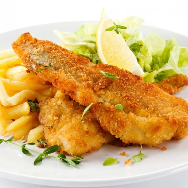 Crispy fried fish fillets with golden french fries, fresh lettuce, and a lemon wedge on a white plate.