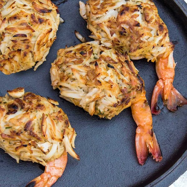 Four shrimp stuffed with crab meat, grilled to a golden brown, on a dark cast iron pan.