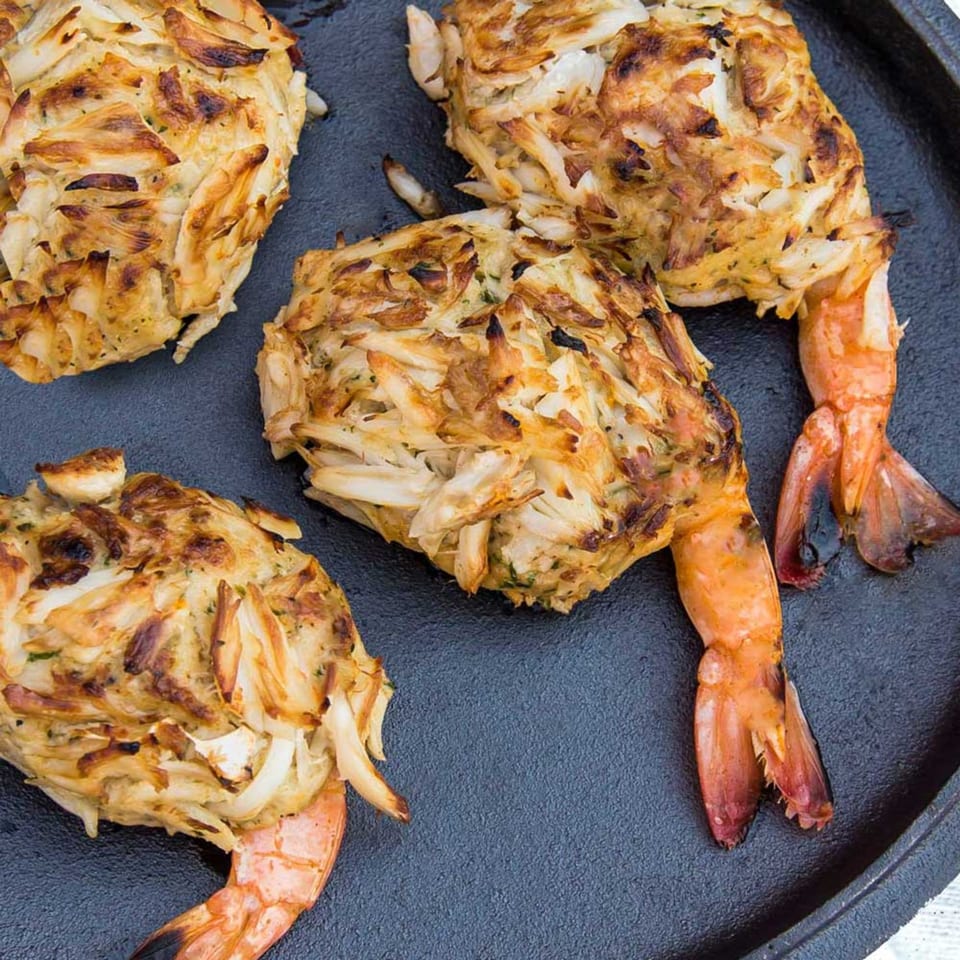 Four shrimp stuffed with crab meat, grilled to a golden brown, on a dark cast iron pan.