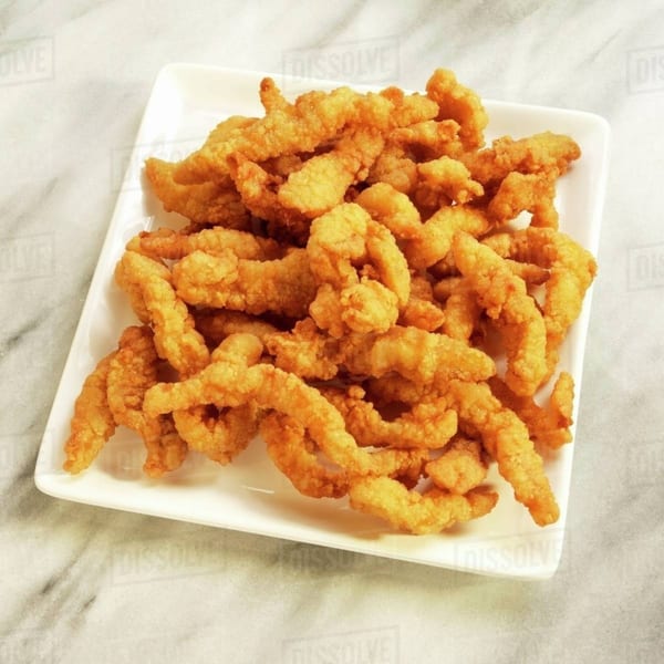 A white rectangular plate filled with golden-brown fried clam strips on a marble surface.