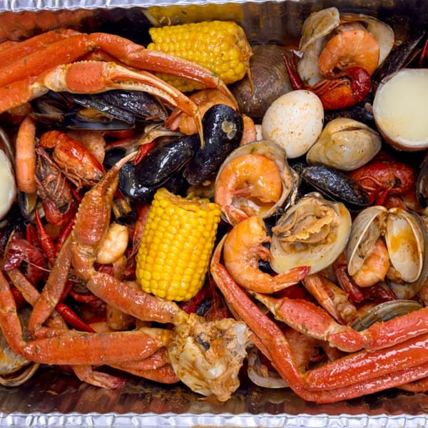 Close-up of a seafood boil with crab legs, shrimp, mussels, clams, corn, and eggs in a foil pan.