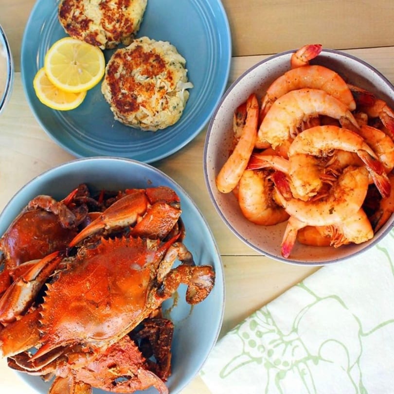 Cameron's Seafood crab cakes with lemon, steamed shrimp, and whole steamed crabs on a wooden table.