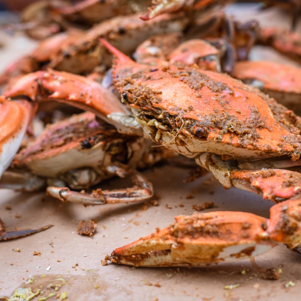 Close-up of several steamed blue crabs, seasoned with spices, on a brown paper surface.