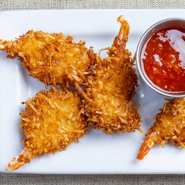 Four crispy coconut shrimp with tails on, served with a side of sweet chili dipping sauce.