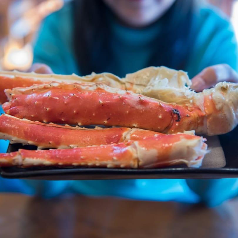 A person holds a black plate piled high with bright red king crab legs, ready to be eaten.