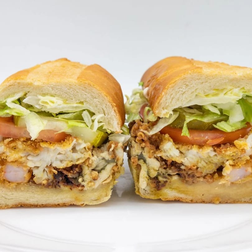 A Cameron's Seafood po'boy sandwich, cut in half, filled with fried seafood, lettuce, tomato, and pickles.