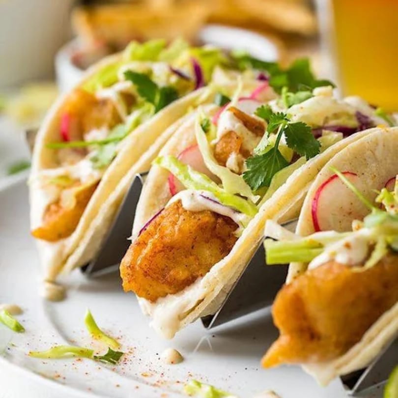Three Cameron's Seafood fish tacos with fried fish, cabbage, radishes, and sauce in a metal holder.