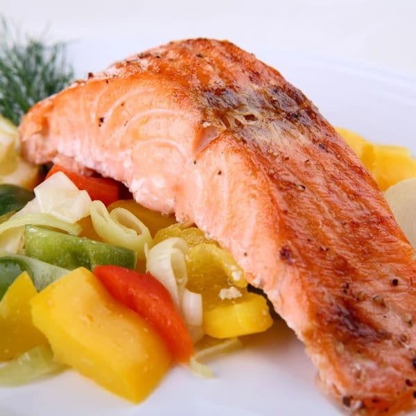 Grilled salmon fillet with colorful bell peppers and onions on a white plate.