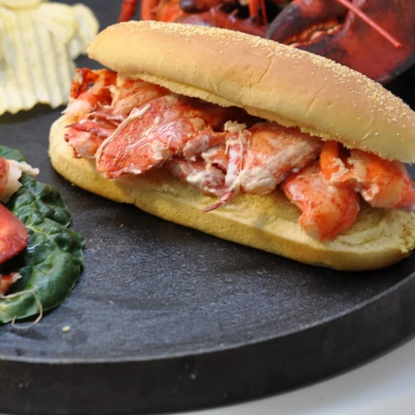 Cameron's Seafood lobster roll with chips and greens on a dark plate.
