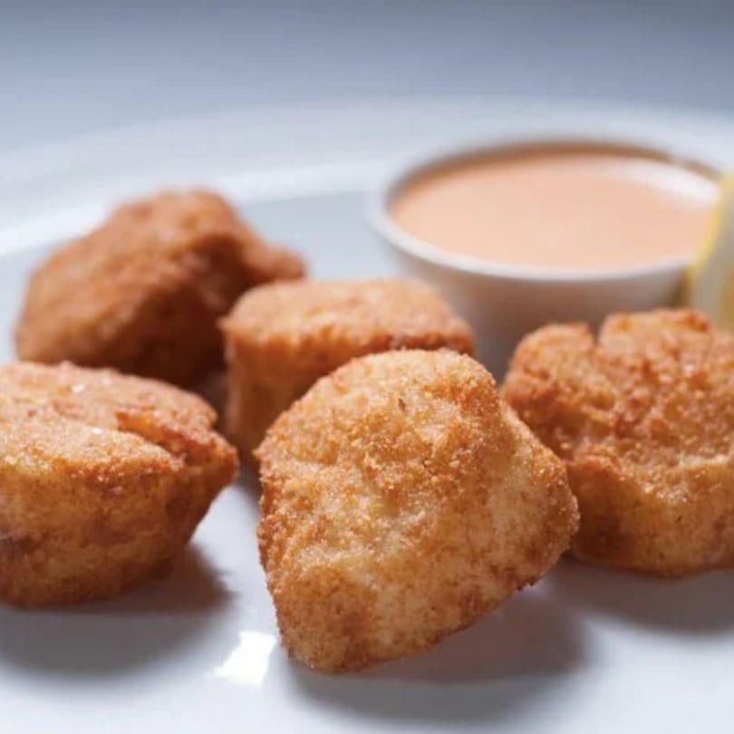 Golden-brown fried scallops on a white plate with a side of dipping sauce and a lemon wedge.