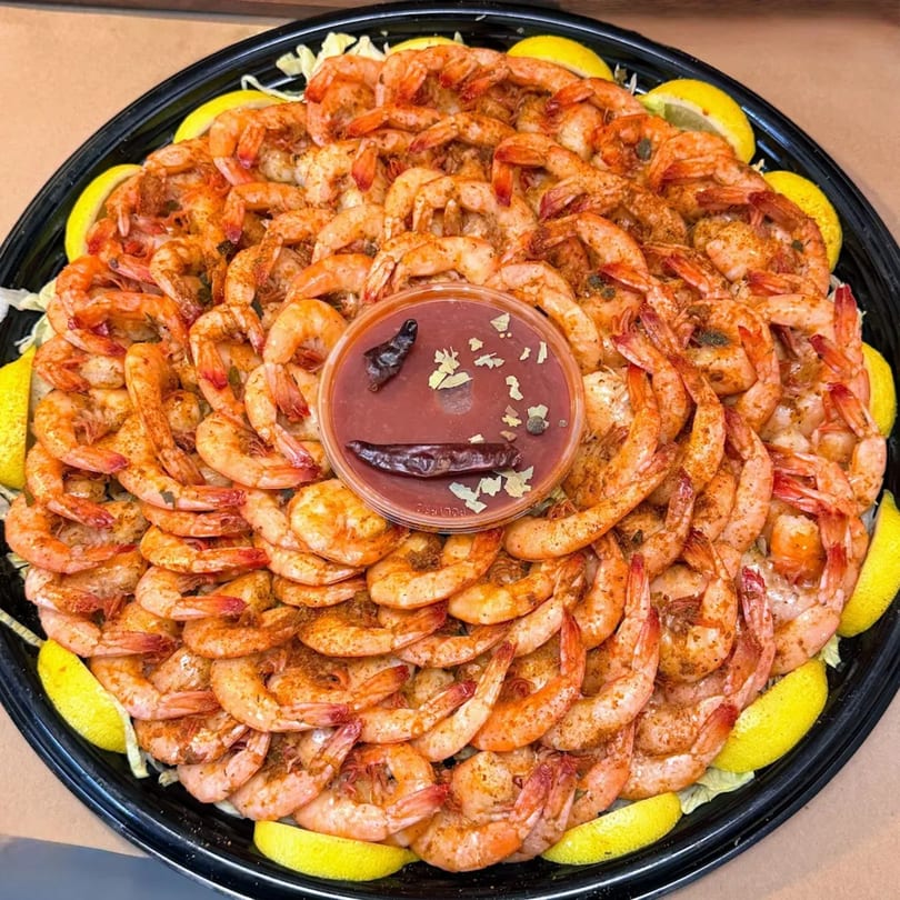 A large platter of seasoned shrimp with lemon wedges and a small cup of cocktail sauce.
