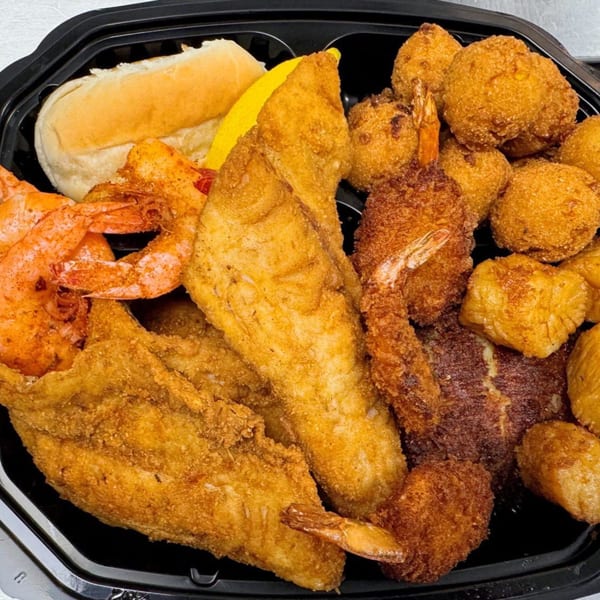 A black takeout container filled with fried fish, shrimp, hush puppies, and a dinner roll.